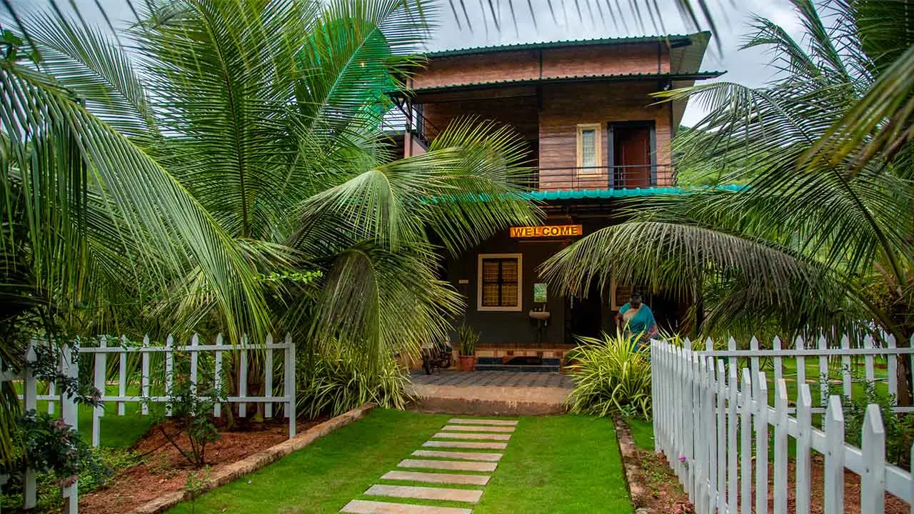 The wooden farmhouse at Jungle Valley Farms framed by coconut palms, with a stepping-stone path across the lawn